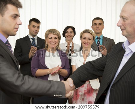 Business award. Mature businessman congratulates younger employee standing in front of the happy team