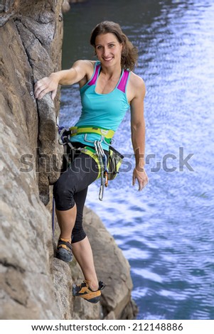 Brave and confident female rock climber enjoys hanging on her hand over the deep abyss. She is smiling and looking straight into camera.