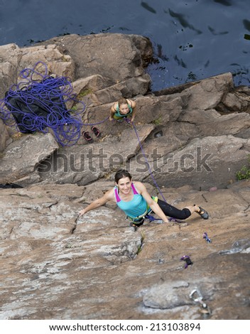 Climbing partners make ascent on to the rock wall. Two female extreme climbers ascending the vertical rock over the rocky beach.
