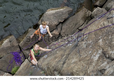 Climbing partners make ascent on to the rock wall Two climbers - male and female - climb rocky wall. They climb over the river rocky beach with impressive stones