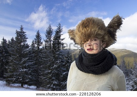 Smiling lady dressed in traditional fur-cap with ear-flaps, snowbound forest and mountains on the background