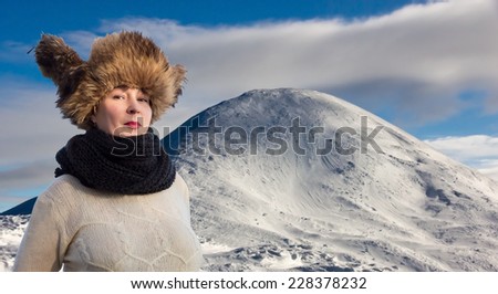 Young smiling female dressed in very warm traditional fur cap and handmade scarf and sweater. Winter landscape on the background