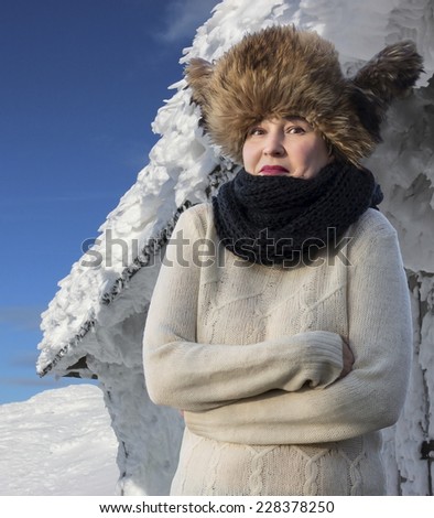 Getting cold! Freezing Caucasian female dressed in traditional warm fur hat and handmade scarf stays in front of polar hut covered by deep ice.