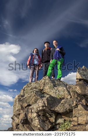 Group of climbers on the cliff. Three alpine climbers with gear stay on the rocky cliff. One male, two females, male is older, looks like father or even grandfather with daughters