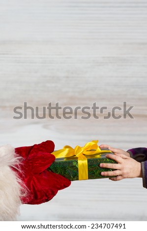 Hands of Santa gives a Christmas gift to hands of child. On wooden background, vertical
