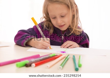 Child rapt with drawing. Child draws the picture using set of colored pens. Focus on hands, pens on the foreground and face are blurred.