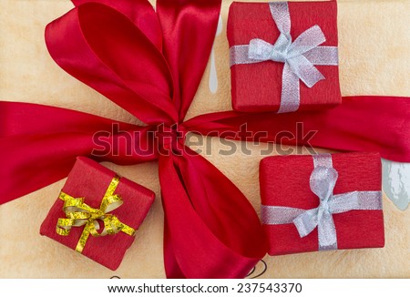 Holidays gifts. Three smaller decoratively wrapped gift boxes located on the bigger box with large red bow-knot