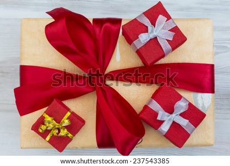 Holidays gifts. Three smaller decoratively wrapped gift boxes located on the bigger box with large red bow-knot, The larger box is on wooden background