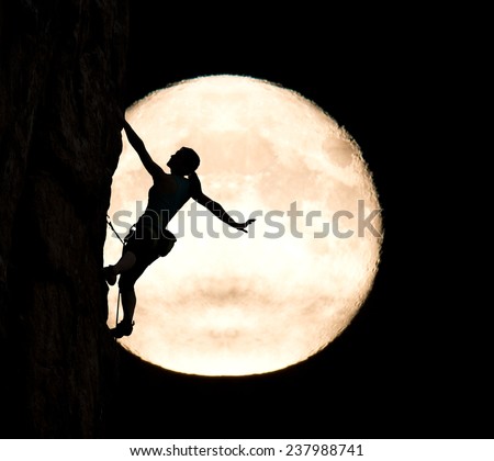 Elegant female extreme climber and big moon. Silhouette of female rock climber hanging on her hand on the vertical rock with big moon on the background