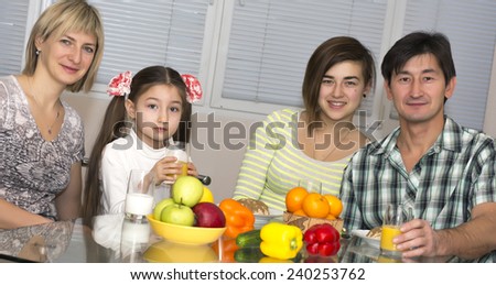 Breakfast of poly ethnic family.  Family of four people has breakfast. People of different nations - Caucasian and Asian, healthy food - fruits, colorful vegetables, juice and milk, modern lifestyle.