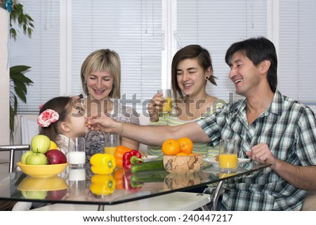 Breakfast of poly ethnic family.  Family of four people has breakfast. People of different nations - Caucasian and Asian, healthy food - fruits, colorful vegetables, juice and milk, modern lifestyle.