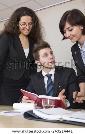 Group of business people discuss working schedule Three young businesspeople, one male and two females, are having discussion with diary, charts and other office supplies