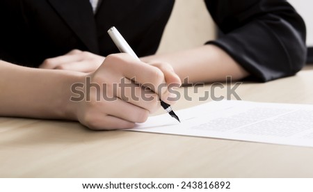 Female businessperson signs contract. Close up of female hand signing formal paper on the office table
