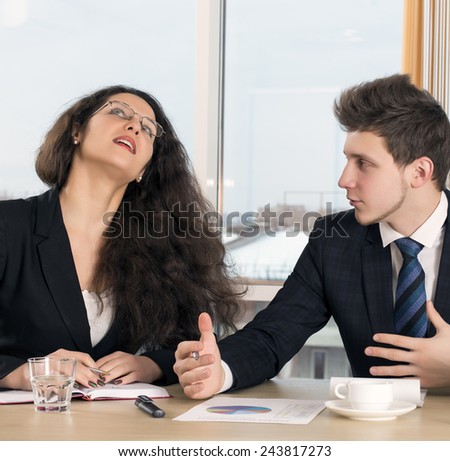 Disagreed female executive and young employee. Bored, disagreed female boss and male businessman who tries to convince her. Office interior, conference table, window on the background