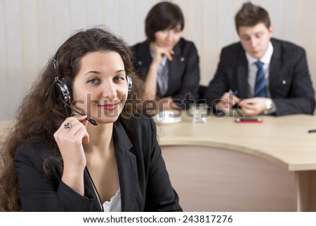 Cheerful female customer support officer. Portrait of smiling cheerful customer support phone operator in headset with her co-workers on the background