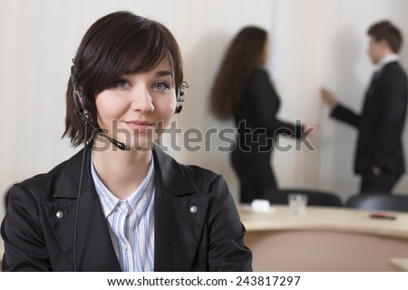 Smiling female customer support officer. Portrait of smiling cheerful customer support phone operator in headset with her co-workers on the background