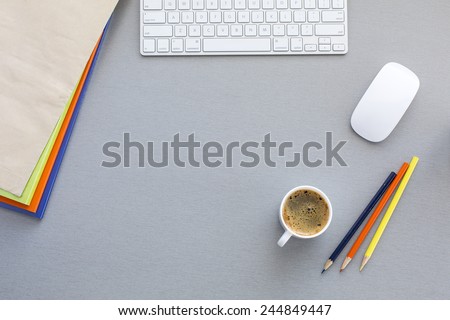 Office work space on grey wood table. From above view on grey wooden working place with colorful booklets, pens, envelope, computer keyboard and mouse and cup of coffee
