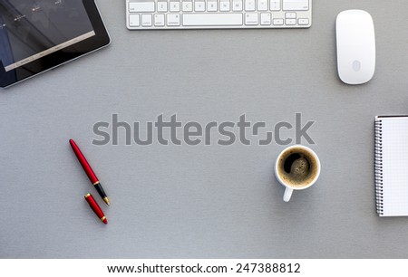 Modern working place on grey wood table. From above view on well equipped working place with tablet PC, computer mouse and keyboard, red pen, cup of fresh coffee, and blank notepad