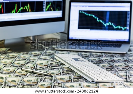 Working place of trader. The table covered by cash notes, keyboard and financial charts on the computer screens