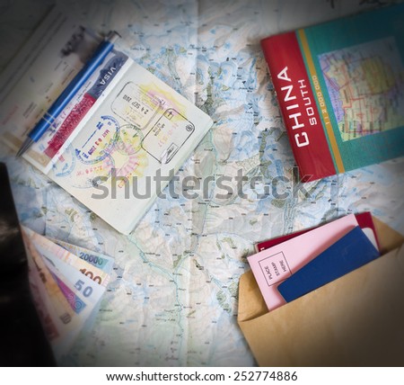 Desk of frequent traveler. The composition of essential items for trip: passport with visa and many stamps, cash notes of different countries, wallet and envelopes, folded map of China and opened map