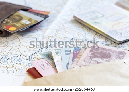 Desk of frequent traveler - angle view. The composition of essential items for trip: passport with multiple entry stamps, foreign cash notes, wallet with credit cards, and map on the background