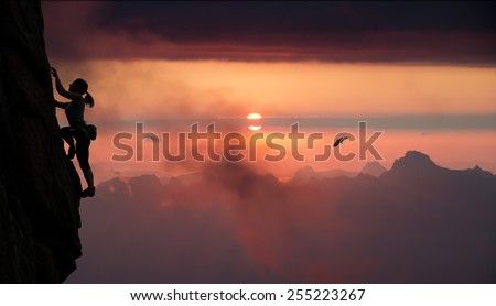 Female rock climber and mountain sunset.\
Silhouette of elegant female extreme climber surrounded by alpine landscape with lake and bright red sunset.