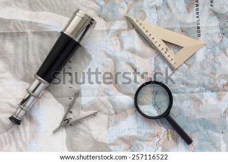 Desk of explorer. Top view of desk covered with the topographic map with typical items of pioneer-navigator: sea telescope, navigational triangle, magnifier and compass