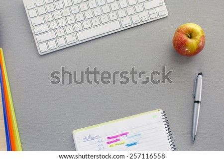 Office work space on grey desk with green apple. From above view on grey wooden desk with well organized office supplies and red apple. Notepad with hand notes marked with bright colors