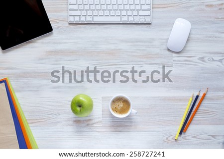 Coffee break.\
Well organized workspace on the wooden table with tablet PC, keyboard and mouse, color pencils, coffee mug along with green apple and some booklets