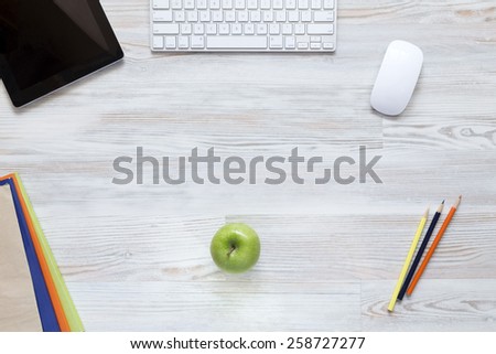 Business lunch.\
Green apple in the middle of well textured wooden desk surrounded with booklets, pencils, tablet PC and keyboard.