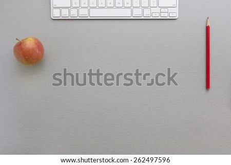 Working space in grey-red. Creative office style composition with red apple, keyboard and red pencil located on grey wooden desk. Top view.