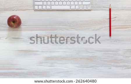 Stylish working desk. Well-textured wooden working desk with red apple and pencil and computer keyboard.