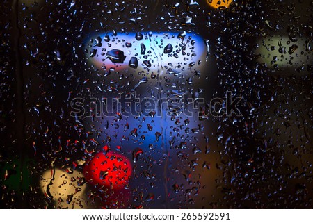 Raindrops on the window with urban night lights.\
Drops and trickles of rain on the window. Colorful night city lights on the background