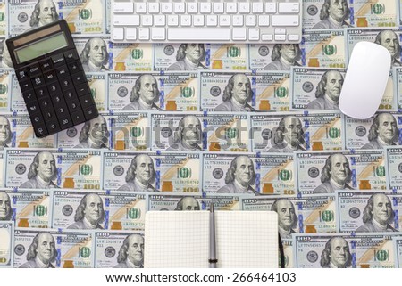 Working place of money maker.\
View from above on the desk covered with the layer of US hundred cash notes with white keyboard, mouse, calculator and note pad
