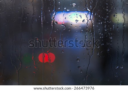 Rain drops on window - night light.\
Drops and trickles of water on glass surface, blurred urban background, colorful neon lights