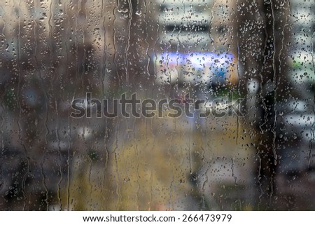 Rain drops on window - evening light.\
Drops and trickles of water on glass surface, blurred urban background, colorful neon lights