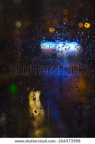 Rain drops on window - night light.\
Drops and trickles of water on glass surface, blurred urban background, colorful neon lights. Vertical composition