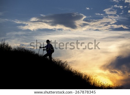 Hiker walks along the slope. Silhouette of human approaching to summit against colorful sunset