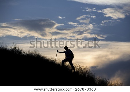 Hiker walks along the slope. Silhouette of human approaching to summit against massive clouds