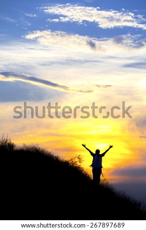 Silhouette of woman with raised hands. Colorful sunset and human body in worshiping posture on the grassy ridge