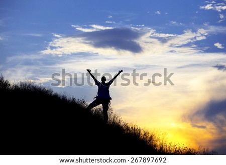 Silhouette of woman with raised hands. Colorful sunset and human body in worshiping posture on the grassy ridge