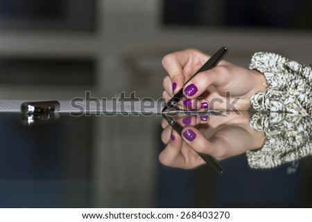 Lady signs contract.\
Close up of female hand signing formal paper on the glass table. Dark background, high contrast