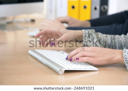 Female fingers typing on keyboard. Office desk with keyboard and some other office supplies, female palms on the foreground, male hands on the background. Fingers of lady with vivid nail make-up