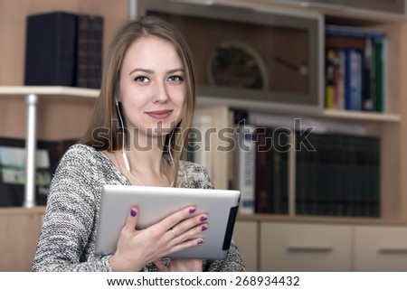 Smiling lady with electronic devise. Portrait of beautiful young woman holding tablet PC. Contemporary home interior on the background, copy space on the right part