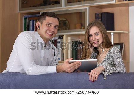 Home entertainments. Young Caucasian man and woman watch movie on the tablet PC. Home interior in warm tone, book shelves on the background, casual dress code
