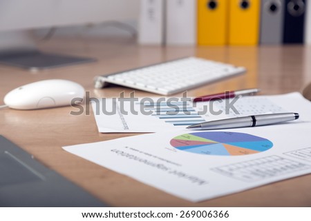 Dropped work. Side view of working place with printed colored charts pens and laptop on foreground cropped big screen and office folders on the background