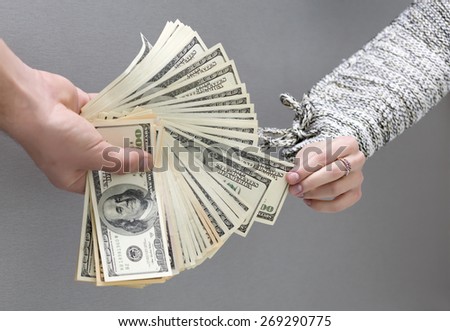 Picking cash note of the hands of husband. Female hand pulls out single cash note from the large stack of notes held by male hand. Caucasian people, grey wooden desk on the background