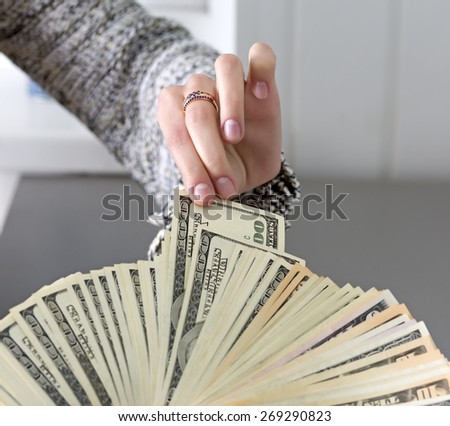 Picking cash note of the hands of husband. Female hand pulls out single cash note from the large stack of notes held by male hand. Caucasian people, grey wooden desk on the background