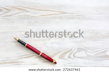 Wooded desk with red stylish pen. From above shoot of part of textured natural wooden surface shape well visible and grey metallic business class red golden pen on the right side copy space available