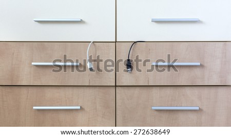 Cabinet with six boxes and black and white cords sticking up. Abstract image of side furniture desk wooden box two light and four dark grey metal handles electronic cord connection white black